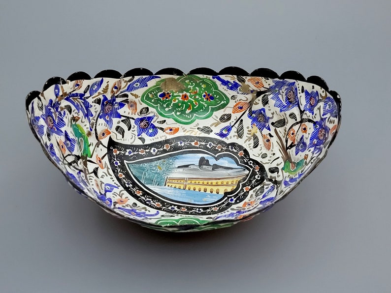 May include: A white ceramic bowl with a scalloped edge. The bowl is decorated with a colorful floral pattern and a scene of a building with arches. The bowl is a traditional design.