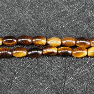 May include: Two strands of polished tiger eye gemstone beads. The beads are oval-shaped with a mix of brown and golden-yellow colors. The beads are strung together, ready for jewelry making or other crafts.