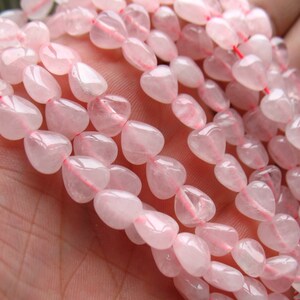 May include: A strand of pale pink heart-shaped rose quartz beads. The beads are smooth and polished, with a translucent appearance.