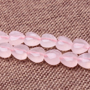 May include: A strand of pink heart-shaped gemstone beads. The beads are strung on a clear thread and are arranged in a double row.
