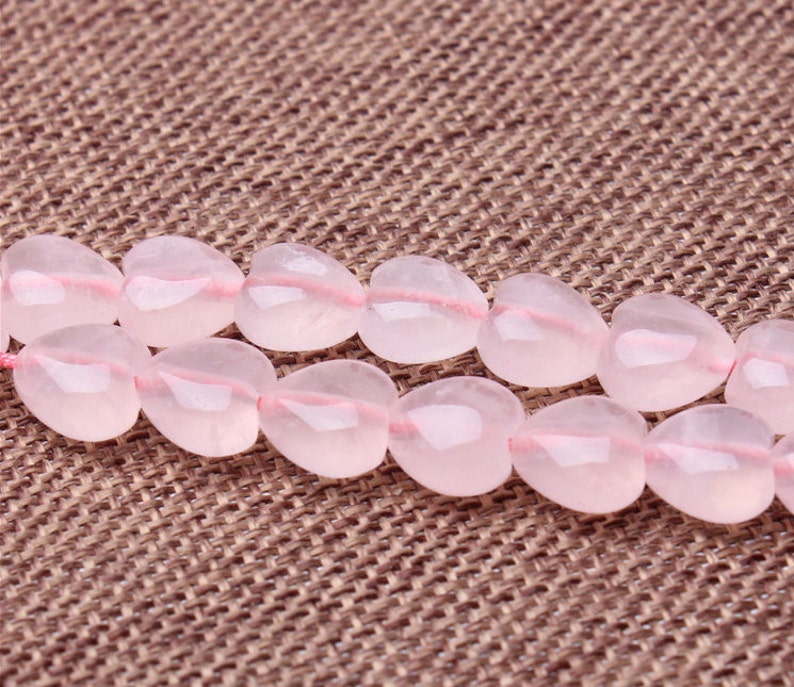 May include: A strand of pink heart-shaped gemstone beads. The beads are strung on a clear thread and are arranged in a double row.