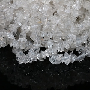 以下が含まれることがあります： ジュエリー作りや工芸品に最適な、透明な水晶チップのクローズアップ。チップは不規則な形で半透明で、わずかな輝きがあります。結晶が積み重なって、質感のある表面を作り出しています。