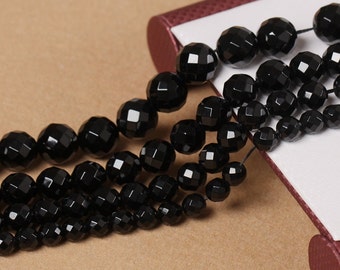 May include: A strand of black gemstone beads, each bead is faceted and has a geometric shape. The beads are strung on a thin cord and are arranged in a loose pile.