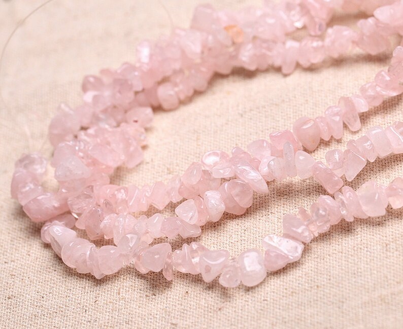 May include: A strand of pink rose quartz chip beads. The beads are irregular in shape and size, and have a natural, unpolished finish.