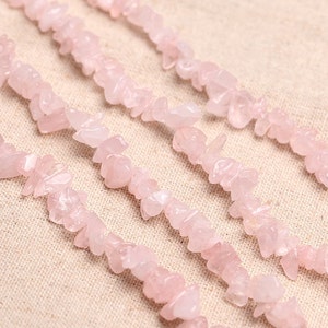 May include: A strand of pink rose quartz chips, also known as rose quartz nuggets, is shown in a close-up image. The chips are irregularly shaped and have a natural, unpolished finish.