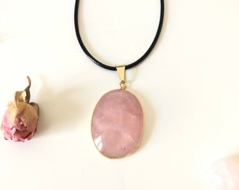 May include: A delicate rose quartz pendant necklace with a gold setting, hanging from a black leather cord.