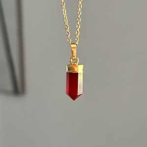 May include: A gold chain necklace with a red carnelian crystal pendant in the shape of a point.