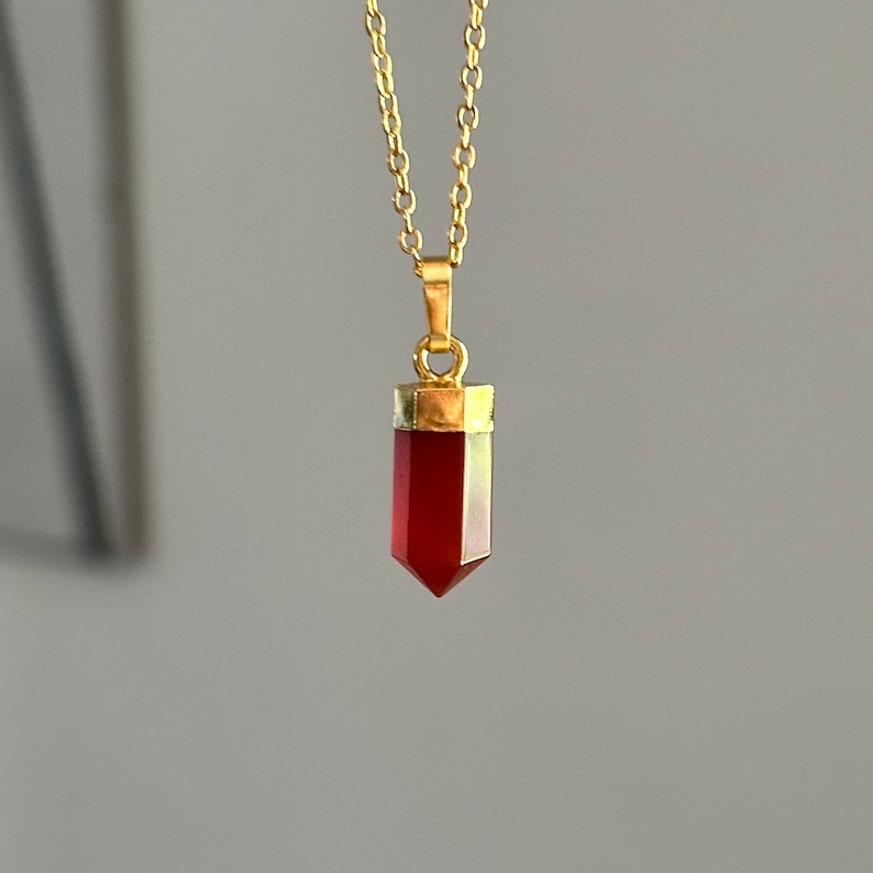 Pendentif en pierre rouge, cornaline facettée avec monture dorée, suspendu à une chaîne fine en or. Bijou minimaliste et élégant, idéal pour un style raffiné