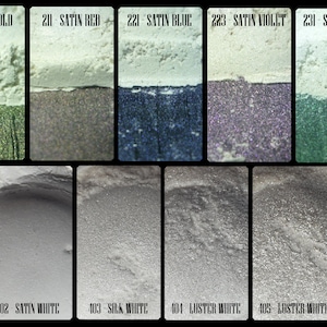 May include: A collection of cosmetic pigments in various colors, including gold, red, blue, violet, and green, with names like "Satin Gold" and "Satin Red." The bottom row features white shades such as "Fine Satin White" and "Glitter White."