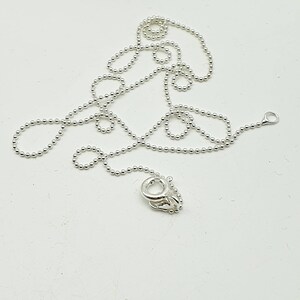 May include: A silver chain necklace with a lobster clasp closure. The chain is made of small, round beads.