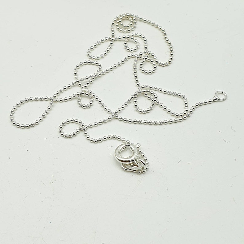 May include: A silver chain necklace with a lobster clasp closure. The chain is made of small, round beads.