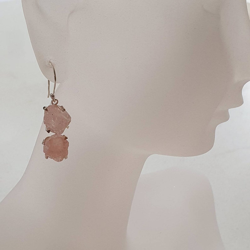 May include: A pair of silver earrings with two pink, rough-cut gemstone drops.