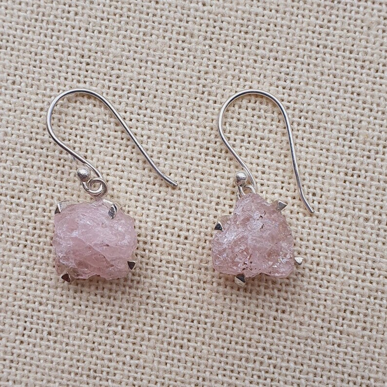 May include: A pair of silver earrings with pink, raw, crystal-shaped stones.