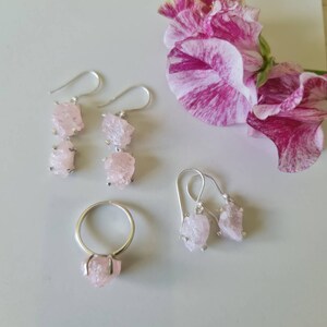 May include: A set of three jewelry pieces featuring pink rose quartz crystals. The set includes a ring and two pairs of earrings.