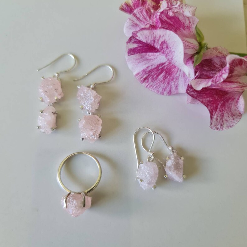 May include: A set of three jewelry pieces featuring pink rose quartz crystals. The set includes a ring and two pairs of earrings.