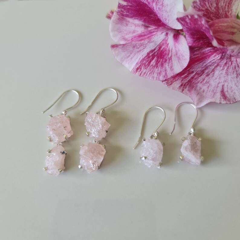 May include: A pair of silver earrings with two pink crystal stones on each earring. The earrings are dangling and have a simple design.
