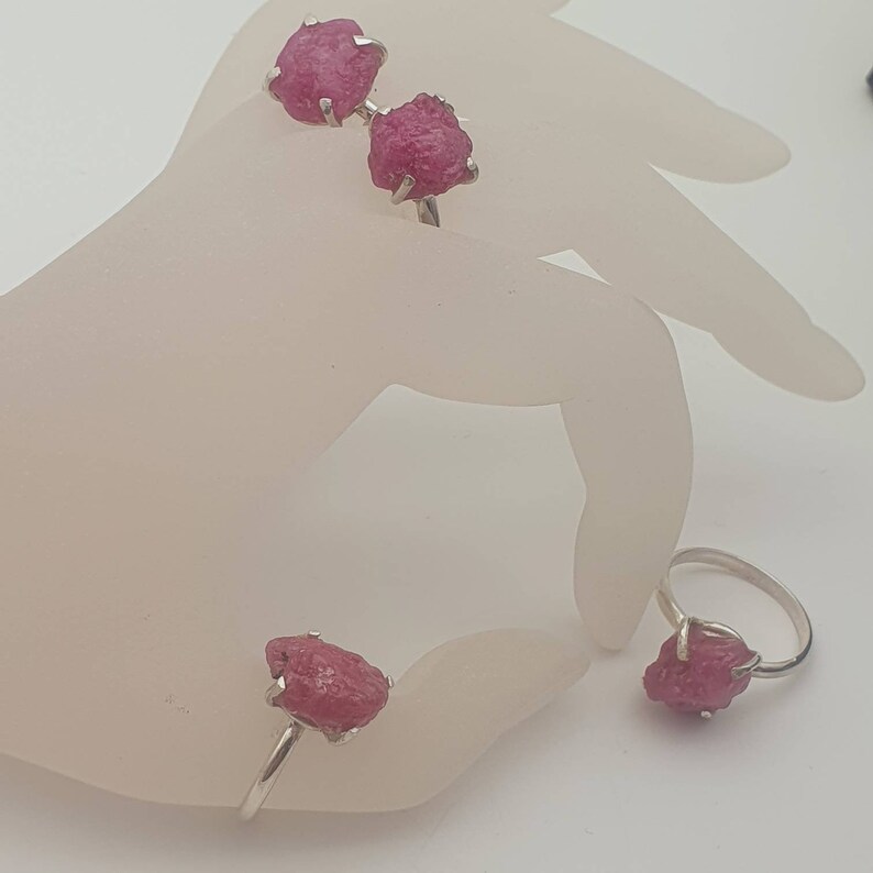 Peut inclure: Trois bagues en argent avec des pierres pr&eacute;cieuses roses brutes. Les bagues sont sur une main de mannequin blanche.