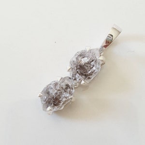 May include: A silver pendant featuring two raw, clear, faceted, and pointed diamonds. The diamonds are set in silver and are connected by a silver chain.
