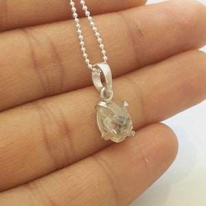 May include: A silver chain necklace with a clear, faceted, rough-cut diamond pendant.