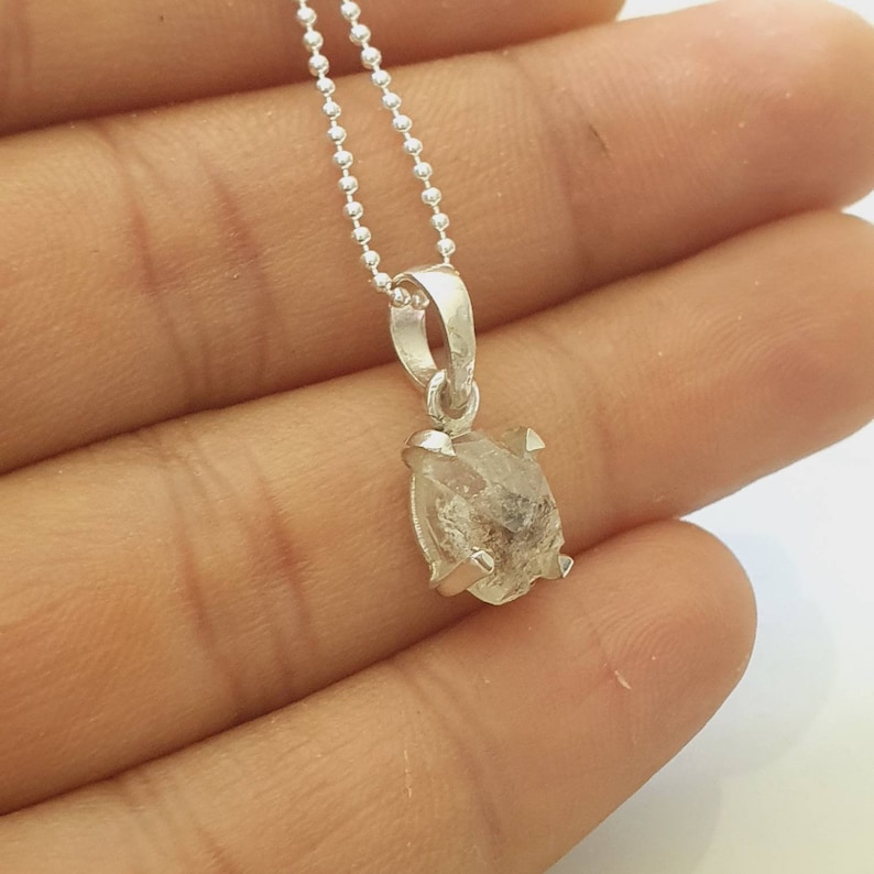 May include: A silver chain necklace with a clear, faceted, rough-cut diamond pendant.