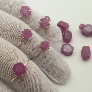 May include: Five silver rings with pink gemstone settings. The rings are displayed on white fabric. Loose pink gemstones are scattered around the rings.