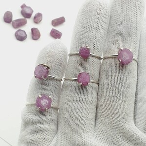 May include: Five silver rings with pink gemstone settings. The rings are displayed on a white fabric background.
