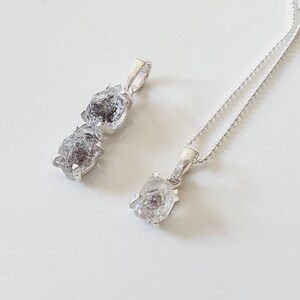 May include: Two silver necklaces with raw diamond pendants. The larger pendant is a double stone, while the smaller pendant is a single stone.