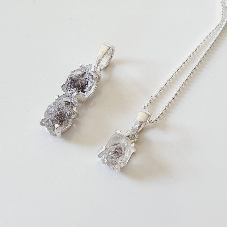 May include: Two silver necklaces with raw diamond pendants. The larger pendant is a double stone, while the smaller pendant is a single stone.