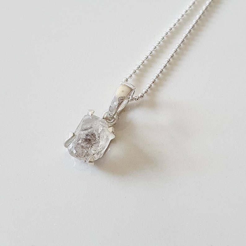 May include: A silver chain necklace with a pendant featuring a clear, faceted, rough-cut diamond.