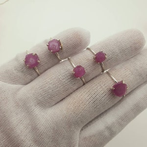 May include: Five silver rings with pink gemstone settings. The rings are displayed on a white fabric surface.