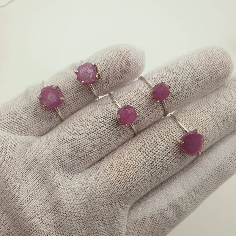 May include: Five silver rings with pink gemstone settings. The rings are displayed on a white fabric surface.