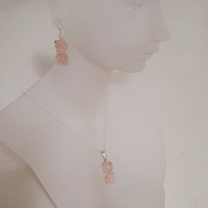 May include: A silver necklace and earrings set with pink rose quartz stones. The necklace features a pendant with two rose quartz stones, while the earrings have two rose quartz stones each.