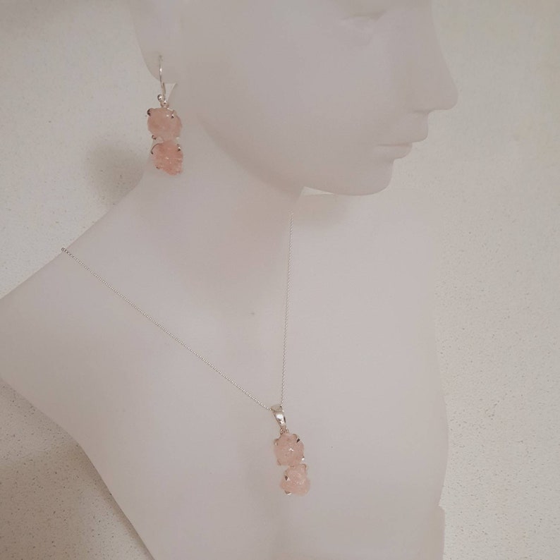 May include: A silver necklace and earrings set with pink rose quartz stones. The necklace features a pendant with two rose quartz stones, while the earrings have two rose quartz stones each.