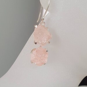 May include: Silver dangle earrings with two pink rose quartz stones. The stones are raw and have a rough, natural texture.