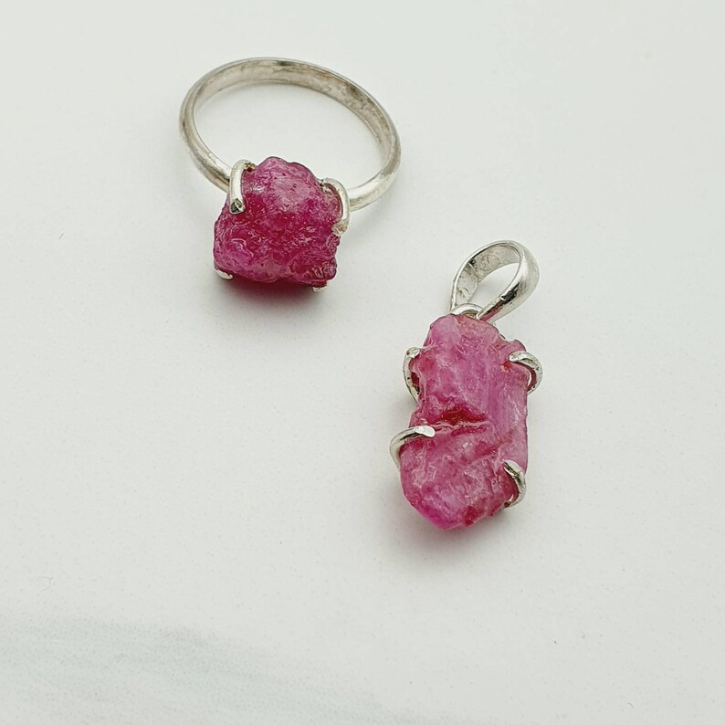 Peut inclure: Un ensemble de deux bijoux en argent avec des pierres pr&eacute;cieuses de rubis rose brut. La premi&egrave;re pi&egrave;ce est une bague avec un gros rubis au centre. La deuxi&egrave;me pi&egrave;ce est un pendentif avec un plus petit rubis au centre.