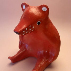 Può includere: Statuetta di volpe rossa fatta a mano con pois bianchi sul muso e sulle orecchie. La volpe è seduta con le zampe distese e ha naso e occhi neri. L'oggetto è decorativo.