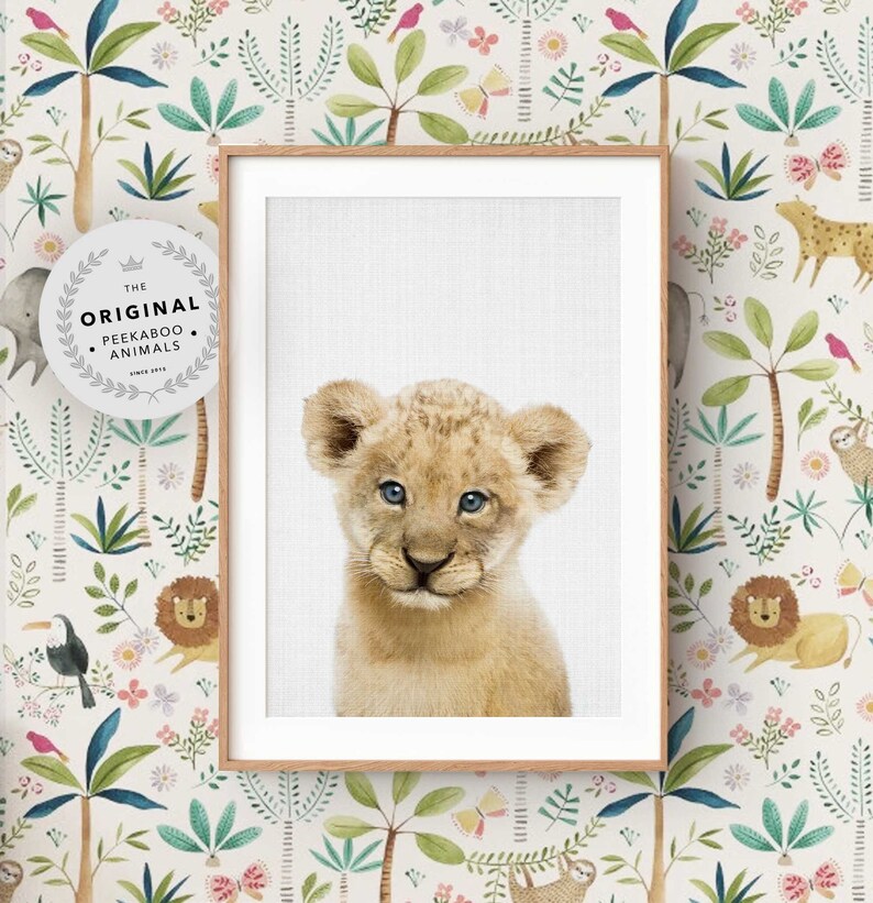 May include: A framed print of a cute lion cub with blue eyes. The print has a white background and is surrounded by a light brown frame. The print is titled "The Original Peekaboo Animals".