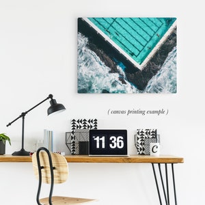 May include: An aerial view of a turquoise swimming pool with white lines, surrounded by dark blue water and white waves. The pool is in the shape of a corner, with the waves crashing against the edge of the pool.