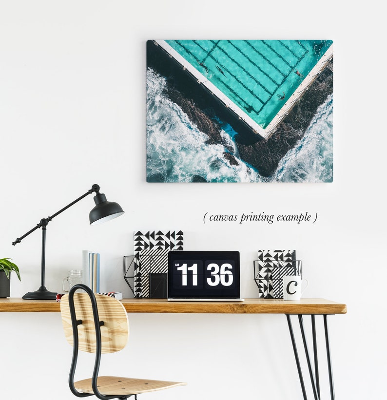 May include: An aerial view of a turquoise swimming pool with white lines, surrounded by dark blue water and white waves. The pool is in the shape of a corner, with the waves crashing against the edge of the pool.
