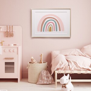 May include: A framed print of a rainbow with pink, brown, green, and blue colors. The rainbow is on a white background. The print is hanging on a pink wall in a nursery.