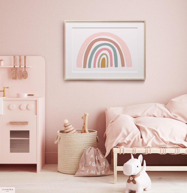 May include: A framed print of a rainbow with pink, brown, green, and blue colors. The rainbow is on a white background. The print is hanging on a pink wall in a nursery.