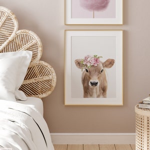 May include: A brown and white calf with a pink flower crown on its head. The calf is looking directly at the camera. The background is white.