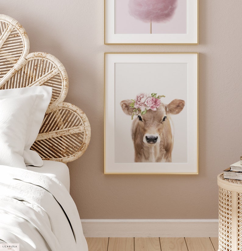May include: A brown and white calf with a pink flower crown on its head. The calf is looking directly at the camera. The background is white.