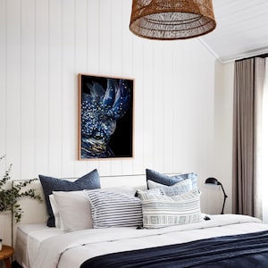 Puede incluir: Una impresi&oacute;n enmarcada de un cacat&uacute;a negro con plumas azules y blancas sobre un fondo negro. La impresi&oacute;n est&aacute; colgada en una pared blanca sobre una cama con ropa de cama azul y blanca.