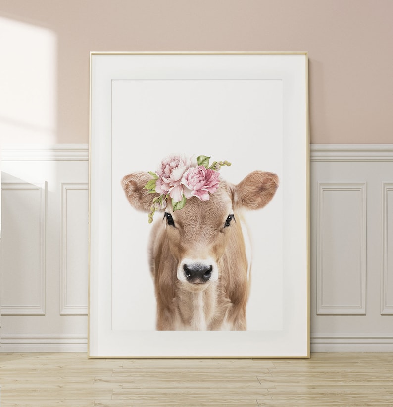 May include: A brown and white calf with a pink flower crown. The calf is looking directly at the camera. The background is white.