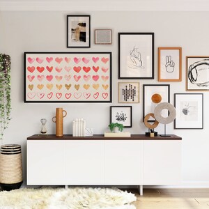 May include: A white cabinet with three doors and a dark brown countertop. The cabinet is decorated with a variety of framed artwork, including a print of hearts, a line drawing of a person, and a peace sign. There are also several decorative items on the countertop, including a vase, a hourglass, and a sculpture.