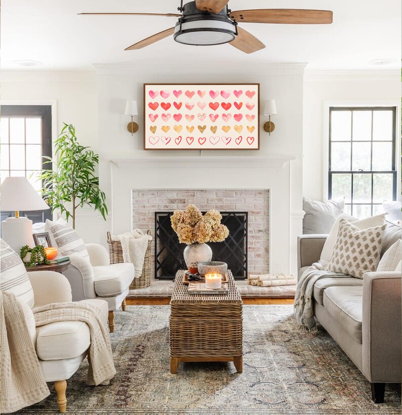 May include: A living room with a white brick fireplace, a white couch, two white armchairs, a coffee table, and a framed print of a watercolor painting of pink and red hearts.