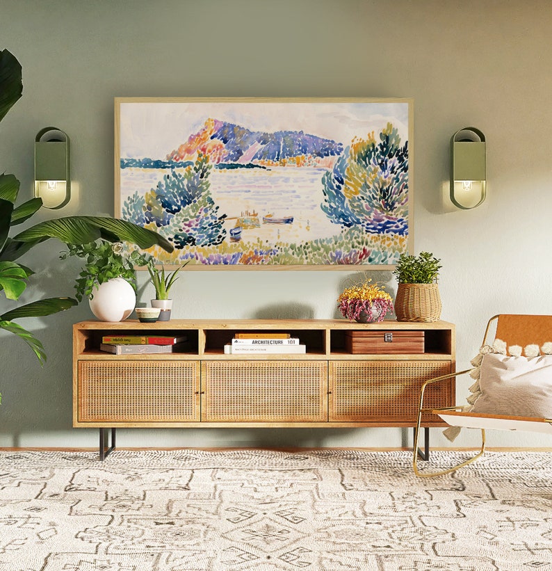 May include: A light green wall with a framed watercolor painting of a landscape with a lake and mountains. There is a wooden cabinet with three doors and a woven rattan front. The cabinet is sitting on a white and gray patterned rug. There are two wall sconces on either side of the painting.