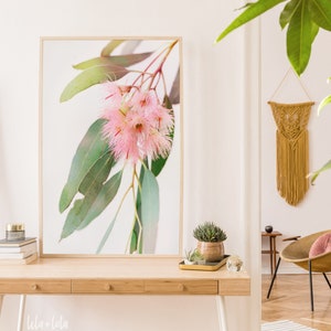 以下が含まれることがあります： 白い背景にピンクの花と緑の葉が描かれた額装されたプリント。プリントは白い壁に木製の机の上にかけられています。