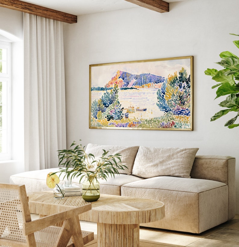 May include: A beige sectional sofa with two pillows sits in a living room with a wooden coffee table and a framed watercolor painting of a landscape with a lake and trees.